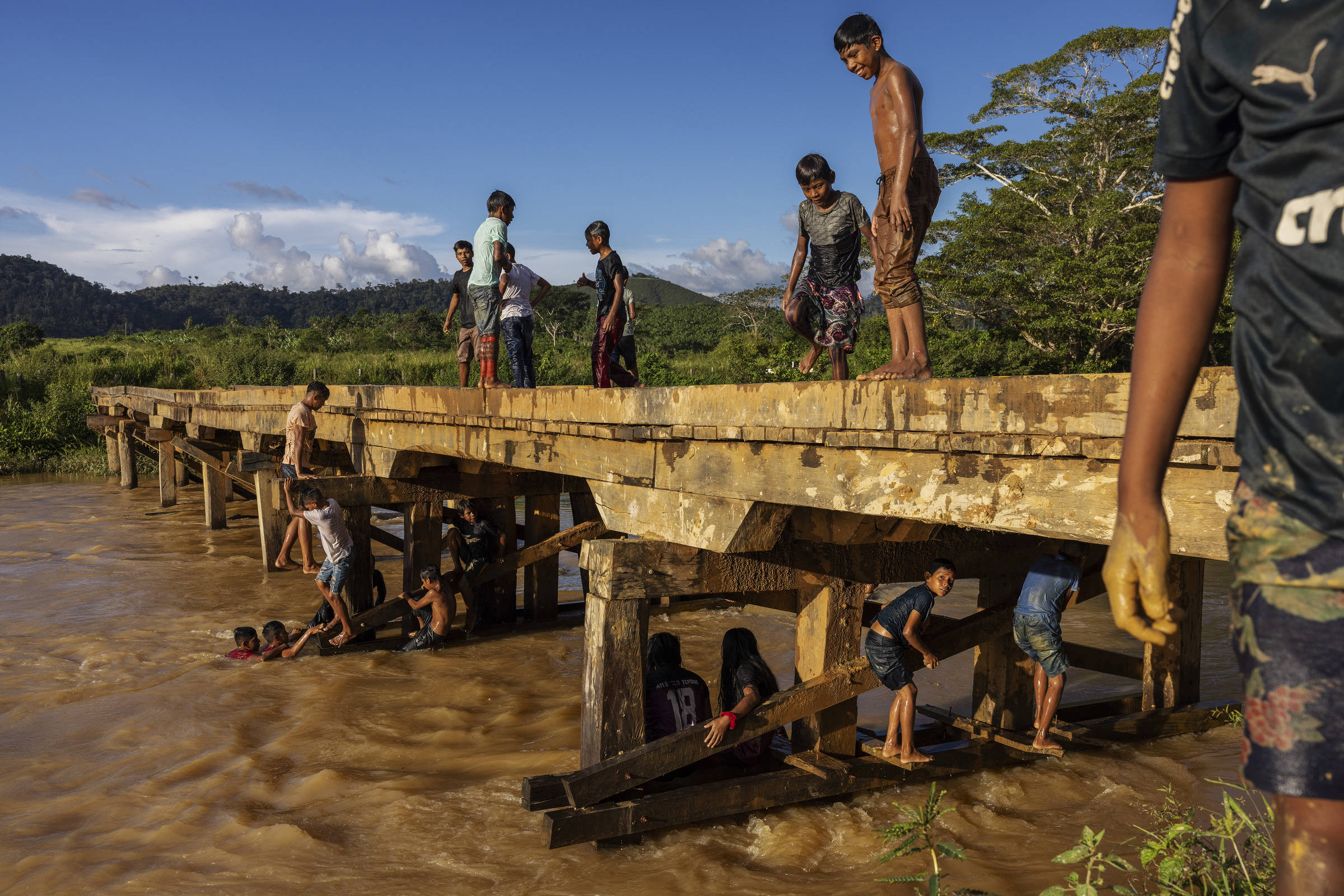 Em uma ponte meninos sorriem com partes do corpo cobertas de lama do rio