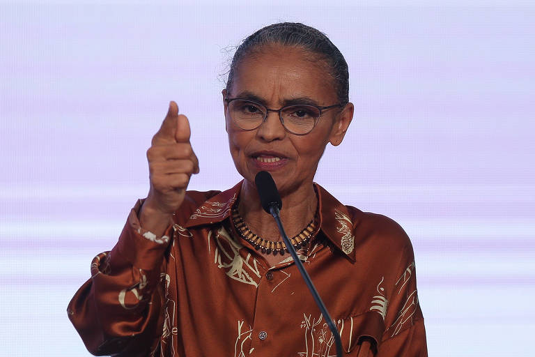 Marina Silva discursa em microfone preto fino e aponta com mão direita e dedo indicador esticado para frente