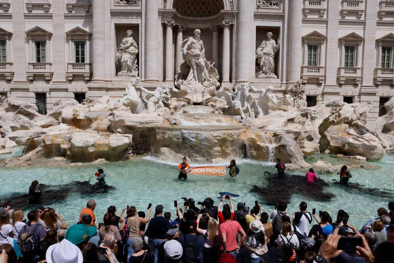 Algumas pessoas estão dentro da Fontana di Trevi, onde parte da água foi tingida de preto em protesto climático