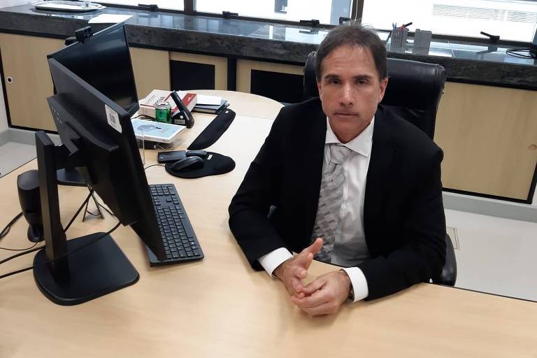 Homem de terno e gravata sentado em frente a computador em sala de trabalho