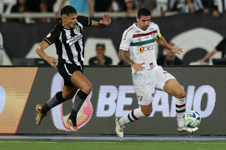 Jogadores do Botafogo e do Fluminense disputam a bola em partida do Campeonato Brasileiro; casas de aposta esportiva aparecem na camisa de ambos e ao fundo, na placa