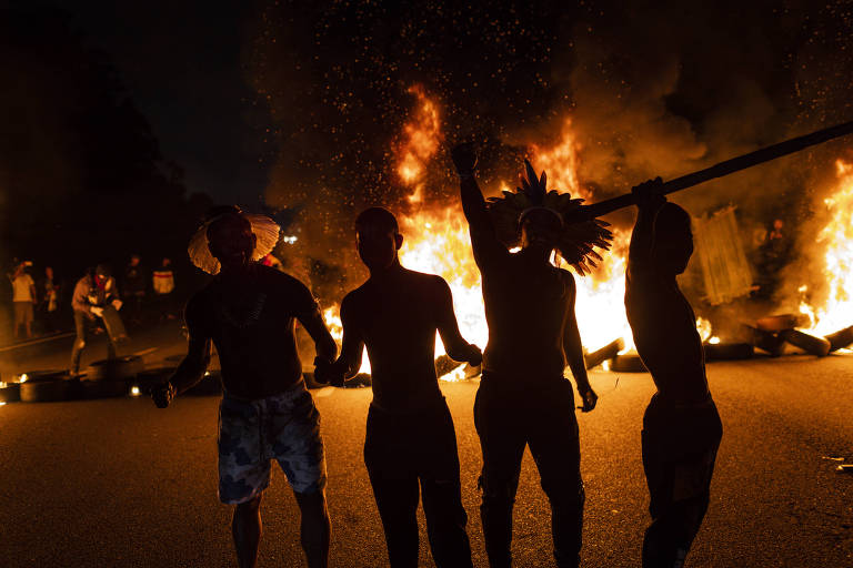 Indígenas são fotografados contra a luz; ao fundo, aparecem chamas de barricadas