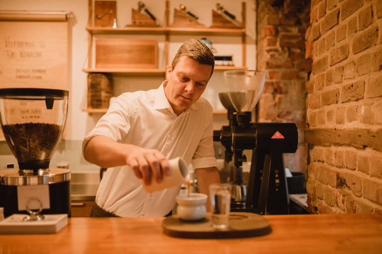 Homem branco com camisa branca serve café em uma xícara