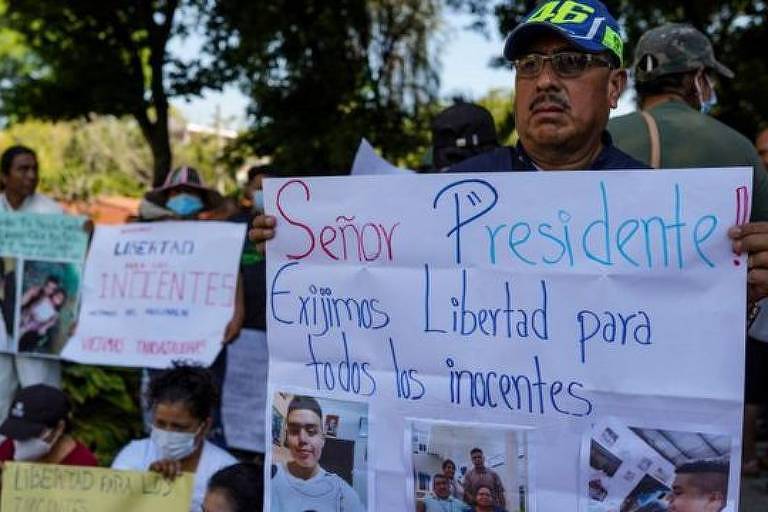 Pessoas segurando cartazes com fotos de detentos