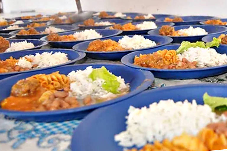 Pratos azuis distribuídos em uma mesa. Dentro dos pratos, arroz branco, feijão, carne e salada verde.