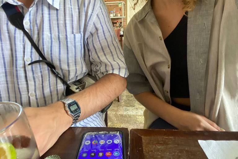 Gabriel Guerra veste o G-Shock clássico por estilo mesmo quando porta seu smartphone. Imagem mostra dois torsos de jovens, um homem e uma mulher. À esquerda está Gabriel Guerra, com camisa listrada e G-Shock no pulso esquerdo. À direita, uma jovem não identificada de blusa preta e camisa caqui