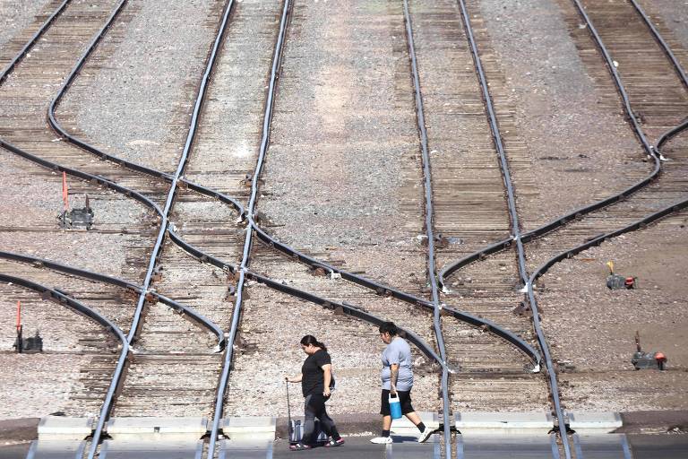 Pessoas carregando galão de água atravessam linha de trem em Phoenix, nos EUA, em meio a uma das piores ondas de calor extremo no país