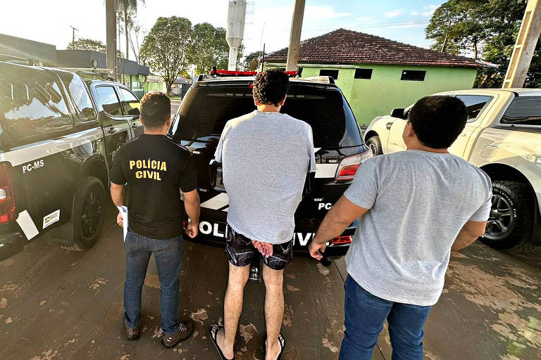 A foto mostra, de costas, o suspeito de matar o jogador de futebol Hugo Vinicius Skulny. Ao lado estão policiais civis que fizeram a prisão do suspeito nesta quarta (16). 