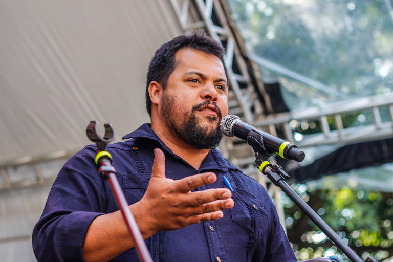 Homem com barba, Diego Moreira, dirigente de produção nacional do MST, fala ao microfone em um evento