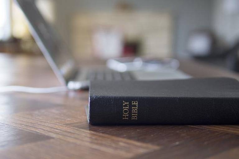 Bíblia em cima da mesa, com laptop atrás