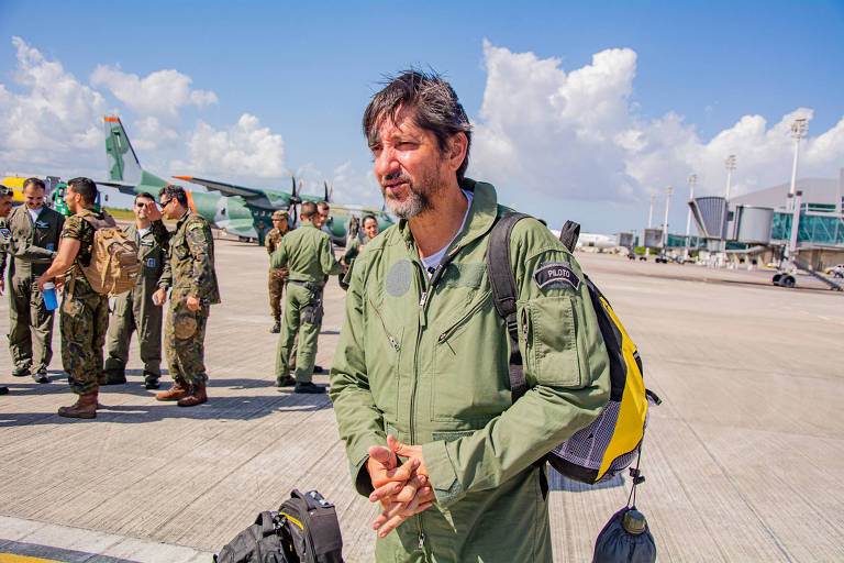 homem de roupa de piloto à frente de outros pilotos e de aviões