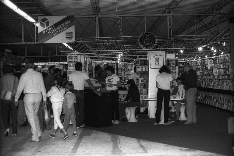 foto em preto e branco mostra pessoas andando entre estandes de livros