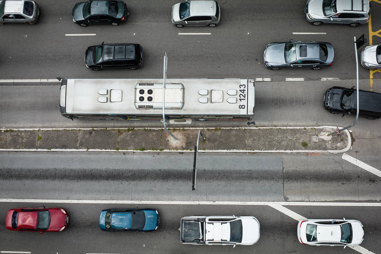 Imagem aérea mostra parte de cima de ônibus e carros em uma avenida movimentada.