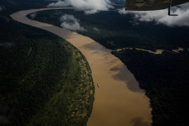 trecho do rio é fotografo de cima; curso d'água está no centro de imagem, com água na cor marrom e há somente uma embarcação