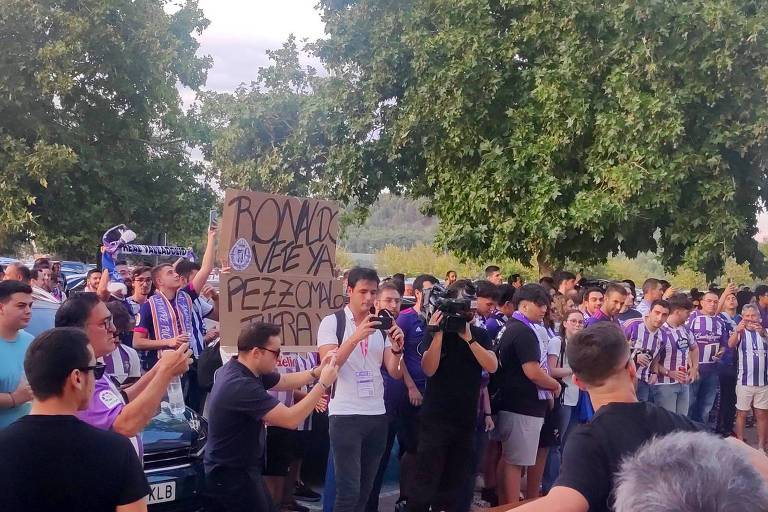 Torcedores do Real Valladolid vestindo camisas branca e roxa do clube com cartazes pedindo a saída do presidente e dono do clube, Ronaldo Nazário, e do técnico Paulo Pezzolano nos arredores do estádio José Zorrilla, na Espanha 