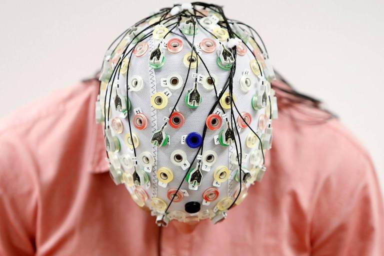 Homem com a cabeça abaixada usa equipamento que mede atividade cerebral
