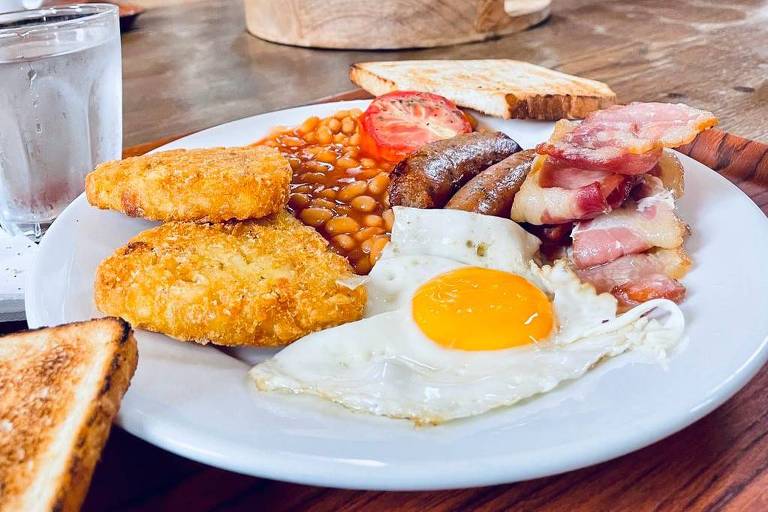 Café da manhã inglês, com baked beans (feijões em molho de tomate), hash browns (batata ralada e frita), ovo, bacon, linguiça e tomate assado