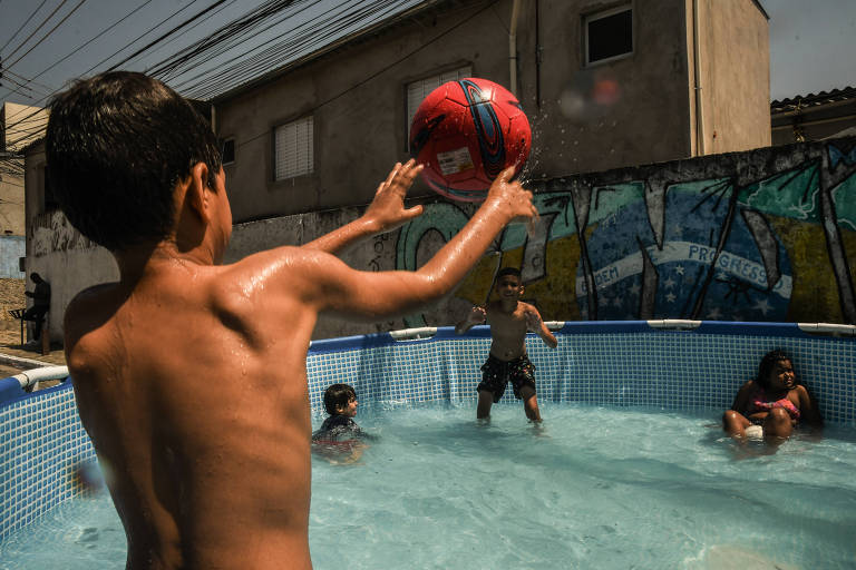 Crianças brincam em piscina de plástico montada na rua por moradora na zona leste de SP 