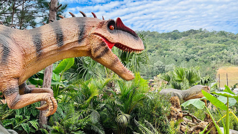 foto de réplica de dinossauro em meio a vegetação artificial