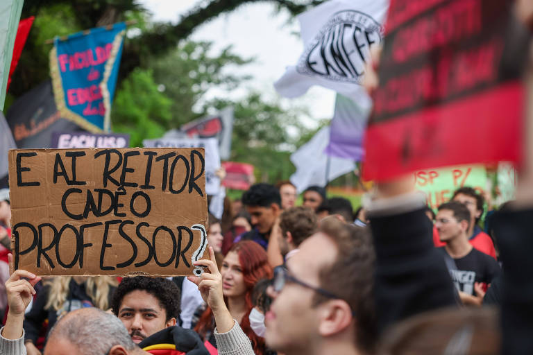 em meio a outros integrantes de manifestação, estudante exibe cartaz de papelão com os dizeres 'e aí, reitor, cadê o professor"