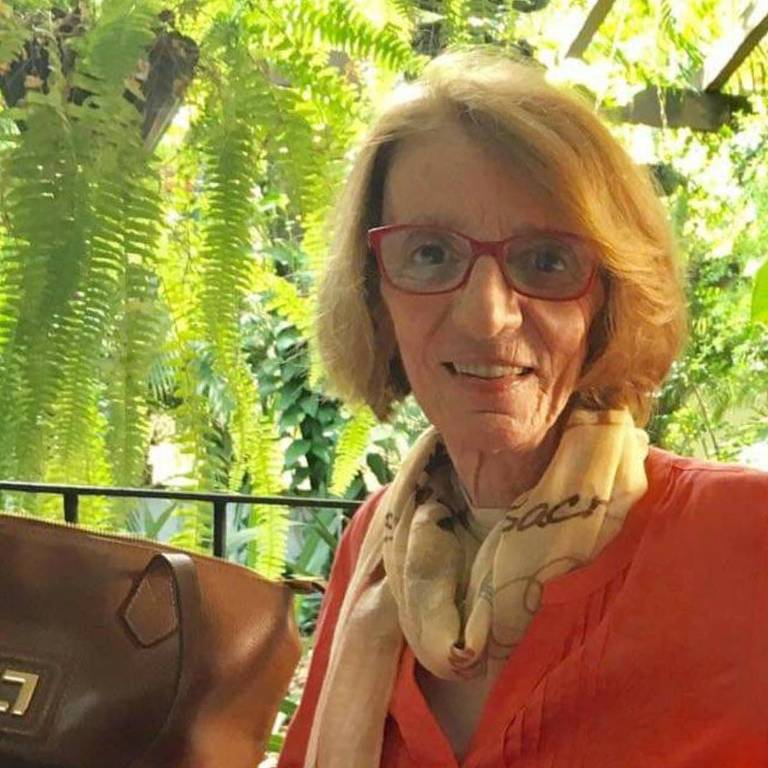 mulher loira de óculos veste casaco laranja em varanda cercada por plantas