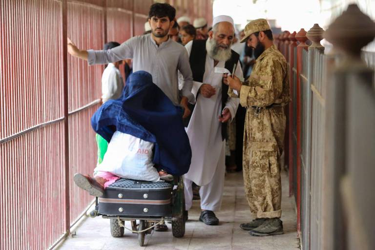 Afegãos cruzam fronteira com o Paquistão enquanto agentes de segurança conferem documentos na região de Torkham