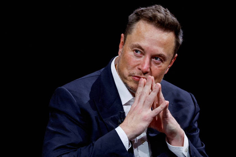 Elon Musk junta as duas mãos e observa com olhar pensativo para o lado direito