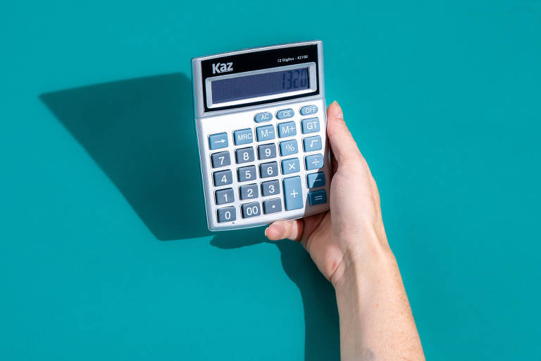 A imagem mostra uma mão segurando uma calculadora sobre um fundo azul. A calculadora é de cor cinza e possui um visor digital e botões numéricos.