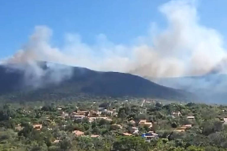 Vista aérea de fumaça ao lado de um morro, perto de casas