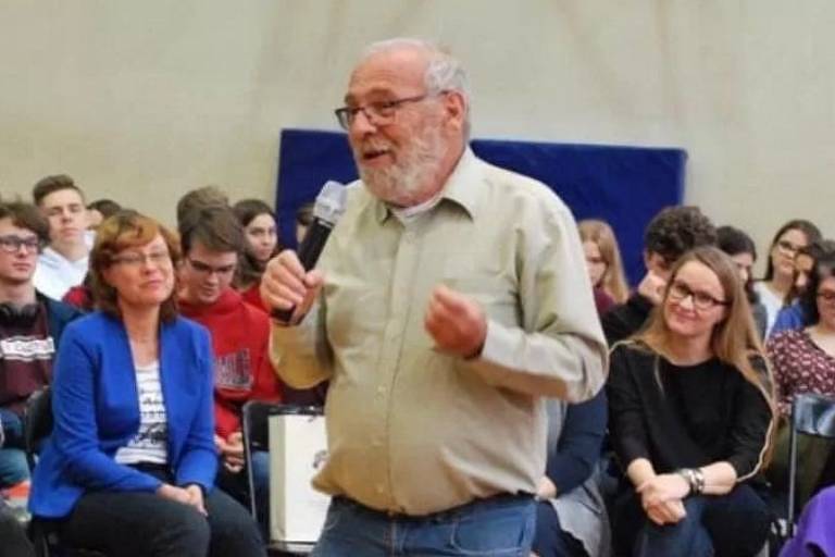 alex fala em aula com microfone na mão direita, atrás dele há pessoas prestando atenção