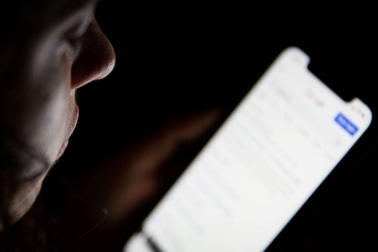 Mulher jovem olha smartphone com tela aberta em pesquisa do Google em sala escura.