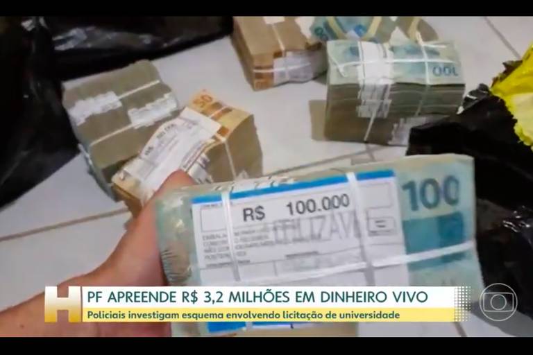 Captura de tela de reportagem com o logo do Jornal Hoje (um H amarelado) com legenda onde se lê "PF apreende R$ 3,2 milhões em dinheiro vivo". Na imagem, uma mão esquerda segura uma pilha de notas amarrada e, ao fundo, outras pilhas. Em primeiro plano, uma pilha com um papel onde se lê "R$ 100.000". No canto inferior direito, logo em marca d'água da Globo