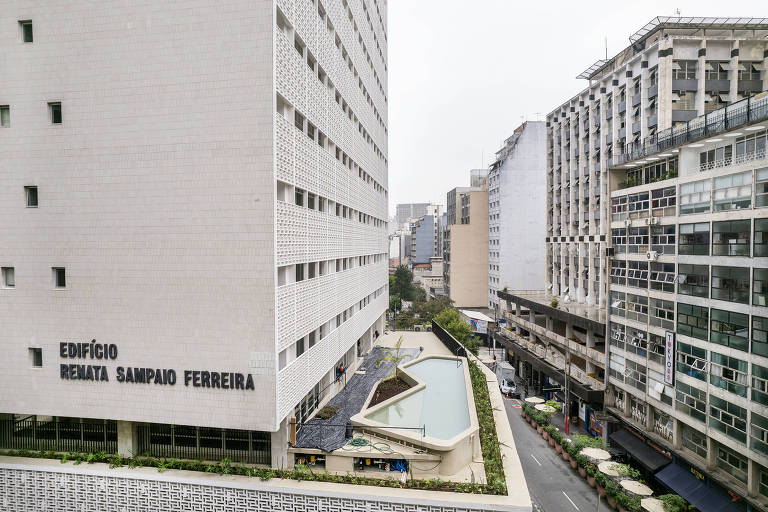 Imagem do alto mostra lateral do prédio branco com uma piscina em sua base, alguns andares acima do nível da rua