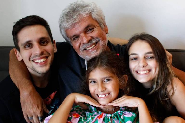 nelson, ao centro, cabelo e barba brancos, é branco, sorri para foto, filhos são brancos com cabelos castanhos e sorriem para foto