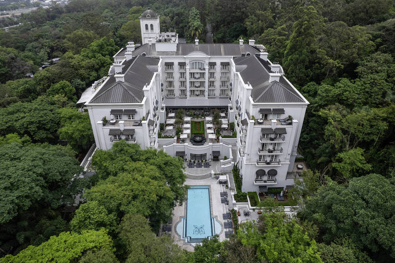 grande hotel na cor branca, com piscina azul, se destaca na mata verde
