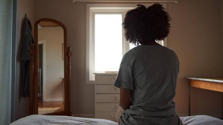 mulher sentada na cama, em frente à janela