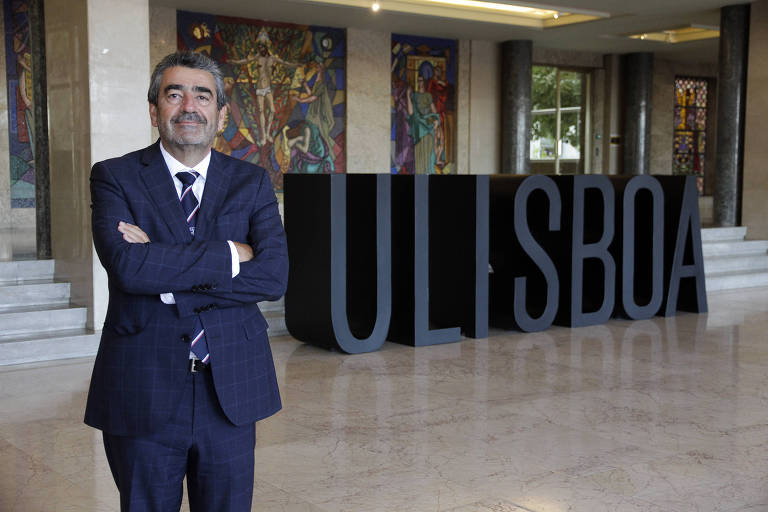 Luís Ferreira, um homem branco, reitor da Universidade de Lisboa. Na imagem ele aparece de terno e gravata, posando em frente a um letreiro com o nome da instituição. Ele está de braços cruzados e tem um leve sorriso