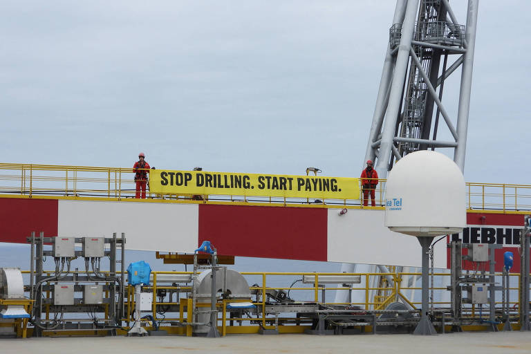 Faixa amarela escrito "stop drilling, start paying" em preto é estendida em navio petroleiro da Shell por ativistas do Greenpeace