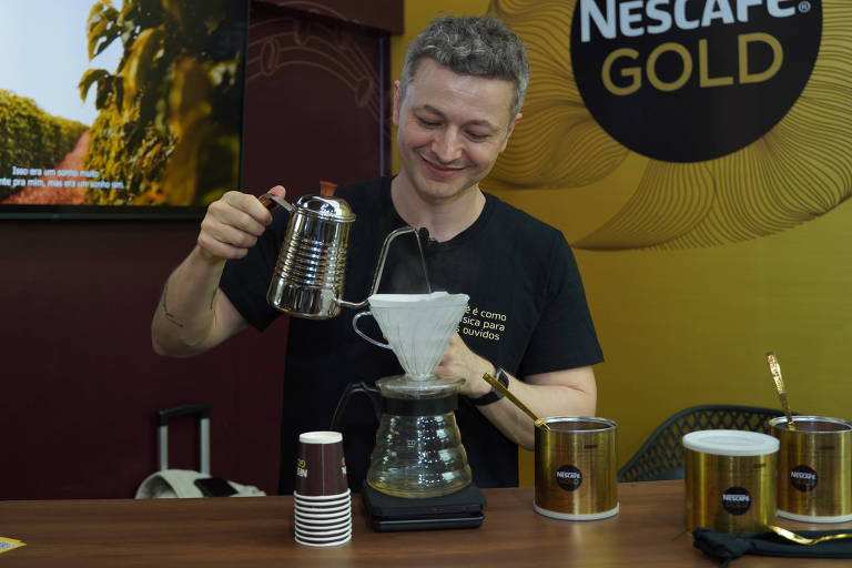 Homem branco de camiseta preta despeja água sobre um coador de café