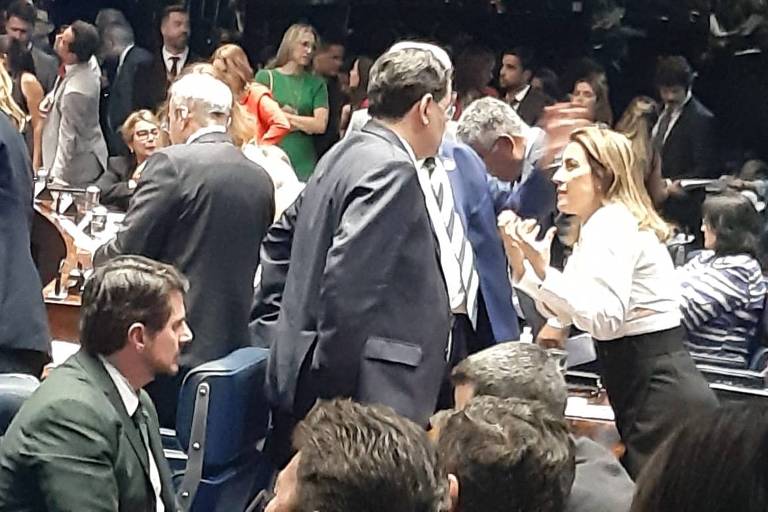 Imagem mostra diversas pessoas no plenário do Senado durante a sessão da Reforma Tributária; algumas estão sentadas, outras em pé