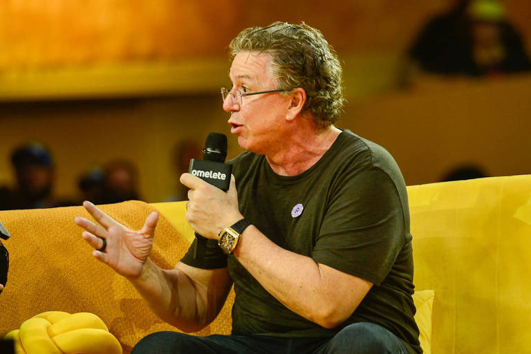 Em foto colorida, homem vestido todo de preto dá entrevista em um estúdio