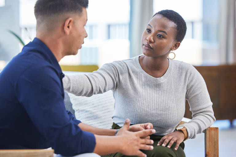 Fotografia mostra uma mulher negra sentada conversando com um homem negro em ambiente de trabalho