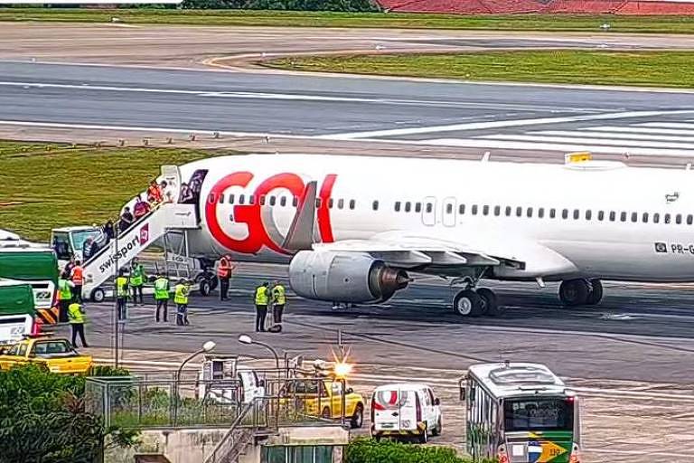 Avião da Gol parado na pista com passageiros descendo por escada na porta da frente 