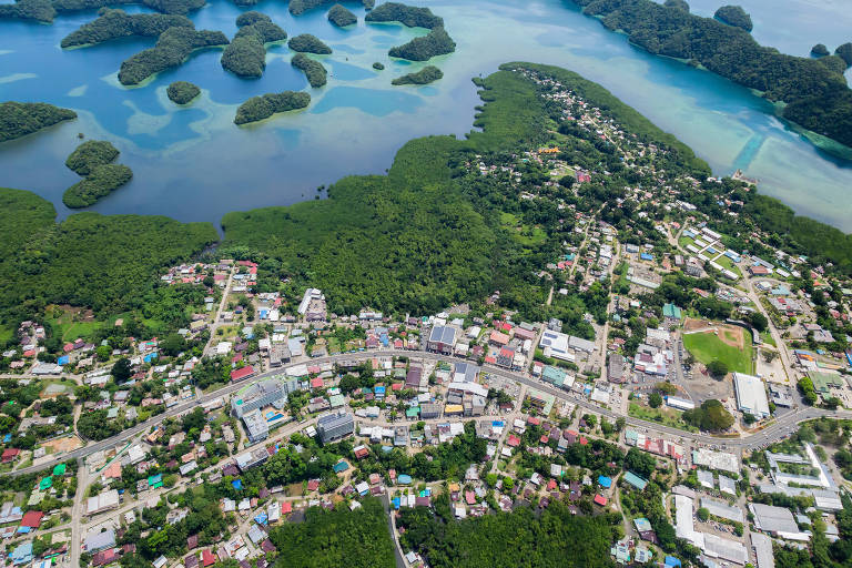 Vista aérea de casas e ruas perto da costa em uma ilha; o oceano é azul claro
