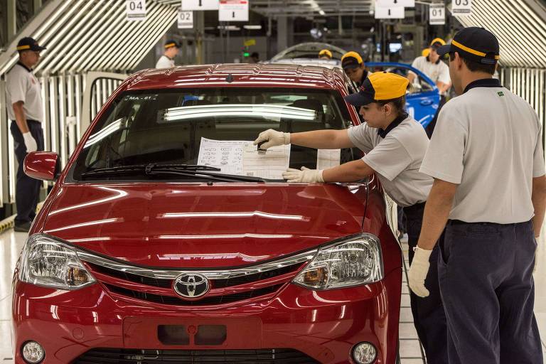 Pessoas colam adesivo de produção em linha de montagem de carros