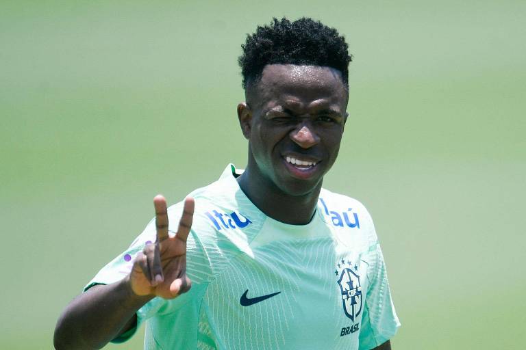 Vinicius Junior exibe os dedos indicador e médio da mão direita e sorri para uma foto em treino da seleção brasileira em Teresópolis, no Rio de Janeiro