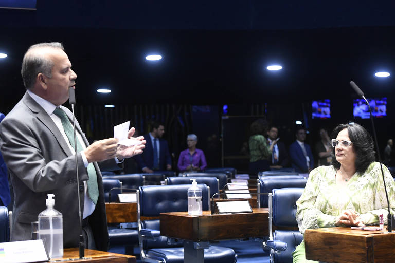 A imagem mostra Rogério Marinho de pé ao microfone e Damares Alves sentada olhando para ele