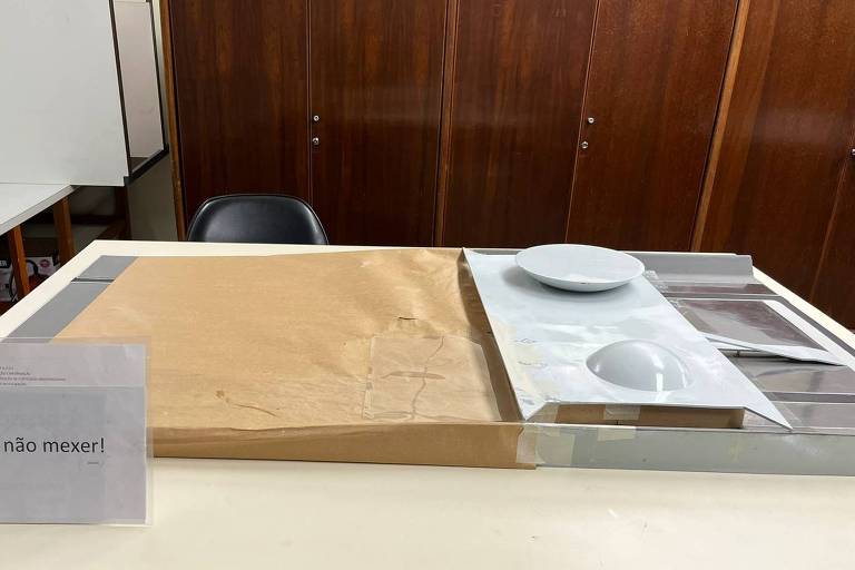 Imagem mostra o que sobrou da maquete tátil do Congresso; objeto está parcialmente coberto por papel pardo. É possível ver apenas as cúpulas da Câmara e do Senado