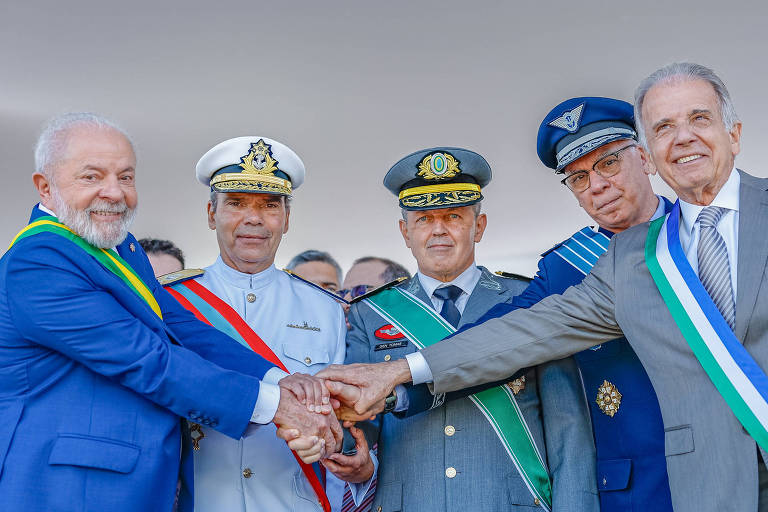 O presidente Lula, de terno azul e faixa presidencial, está de mãos dadas com os comandantes das Forças Armadas e o ministro da Defesa, José Múcio Moneito