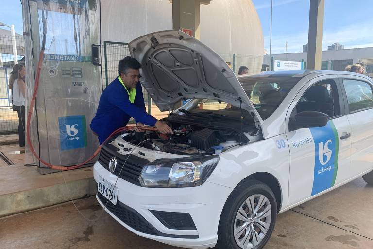 Homem segura mangueiras no motor de um carro com o capô aberto